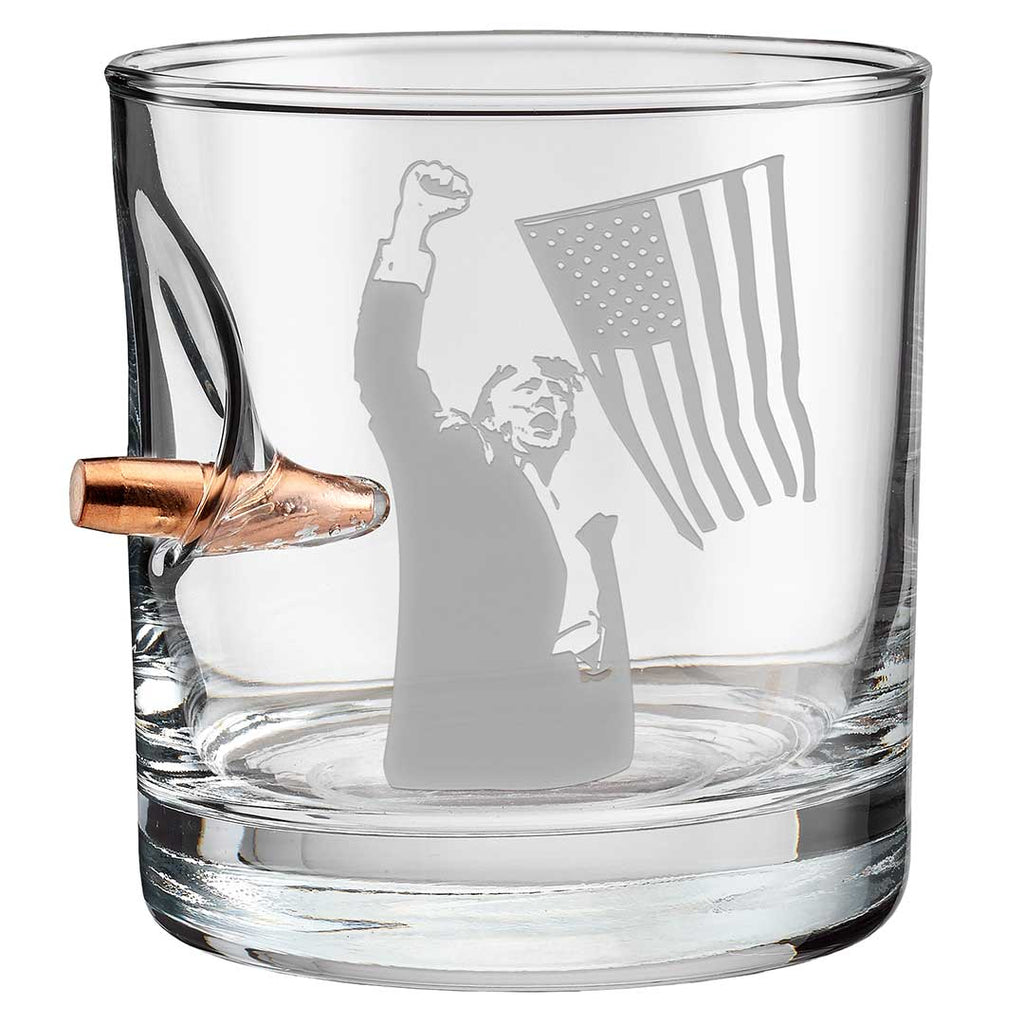Trump whiskey glass featuring an etched design of a figure with a raised fist and an American flag, with a bullet-shaped h...